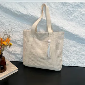 Grand sac cabas tressé beige avec breloque à franges sur fond texturé blanc