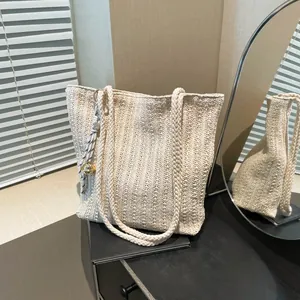 Minimalist straw woven tote bag with shoulder straps and decorative charm tassel