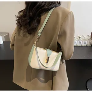 Rear view of model wearing a two-tone beige and green leather crossbody bag with gold clasp