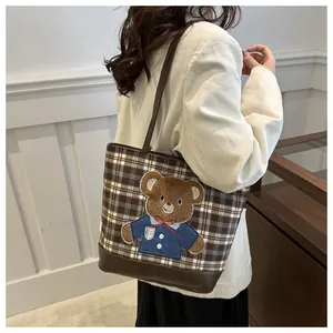 Detail of plaid tote bag with brown teddy bear patch and woven shoulder straps