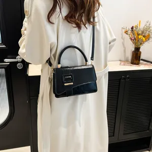 Minimalist black glossy leather handbag with top handle and shoulder strap worn by model