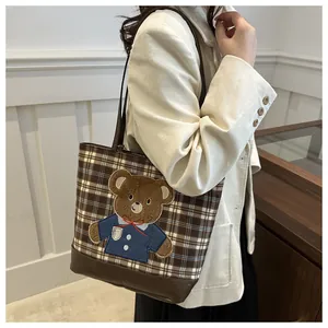 Close-up of brown plaid tote bag featuring a cute 3D teddy bear embroidery and leather straps