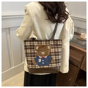 Detail of checkered tote bag with brown leather base and cute teddy bear embroidery