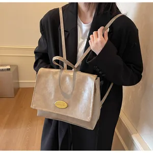 Detail of beige faux leather bag showing polished gold logo plaque and sleek flap texture