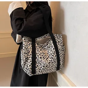 Detail of leopard print tote bag with black straps and side pocket shown on a model