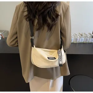 Dettaglio borsa a mezzaluna in pelle crema con tracolla logata e tag FASHION