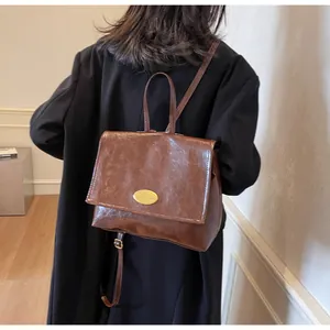 Detail of a vintage dark brown leather backpack with gold logo plate on a model