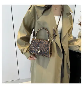 Chic leopard print crossbody bag with gold oval clasp shown on a trench coat model