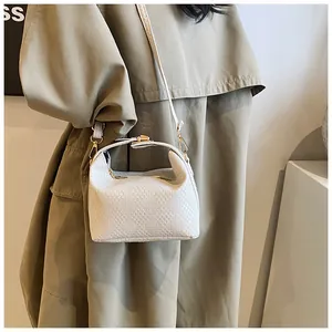 Détail du petit sac tressé avec boucle dorée porté sur un trench-coat beige élégant