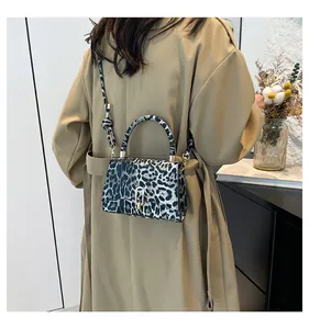 Chic leopard print crossbody bag with gold U-shaped buckle on a model in trench coat