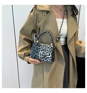 Detail view of leopard print crossbody bag with silver oval lock on khaki trench coat