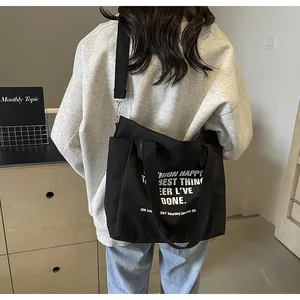 Detailed view of a black canvas tote bag with white lettering worn by a model in casual wear