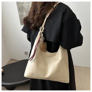 Detalle del bolso tote crema con correa anudada y colgante de osito de peluche marrón