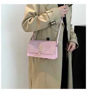 Détail du sac bandoulière rose avec rabat pailleté et pompon doré sur un manteau beige