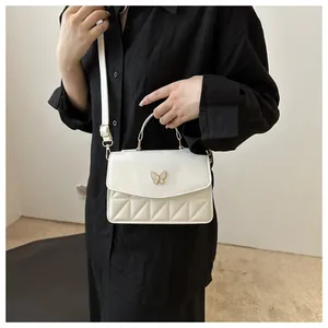 Detail van witte crossbody tas met gouden vlinderversiering en verstelbare schouderband