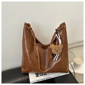 Detalle del bolso tote marrón de piel sintética con un colgante de oso y lazo suave