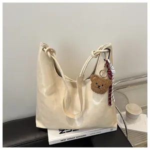 Detalle del bolso tote blanco crema con colgante de oso de peluche y correa anudada