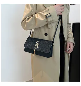 Détail du sac à bandoulière noir avec logo S doré et franges sur un trench-coat