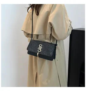 Détail du sac bandoulière noir avec rabat pailleté et logo doré orné d'un pompon