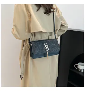 Détail du sac bandoulière en cuir noir avec rabat pailleté, logo S doré et gland en métal