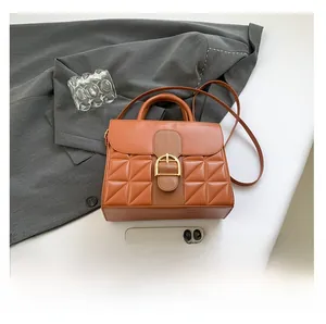 Close-up of quilted orange-brown crossbody bag with golden D-clasp and leather handle