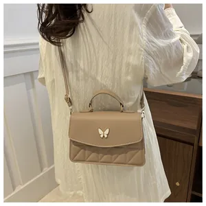 Beige crossbodytas met gewatteerd patroon en vlinderdetail gedragen door een model