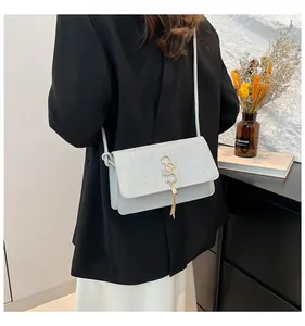 Détail du sac bandoulière à rabat pailleté avec logo S doré et gland à franges
