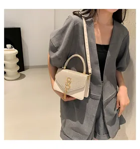 Détail d'un sac bandoulière beige avec boucles dorées et pompon sur un mannequin élégant