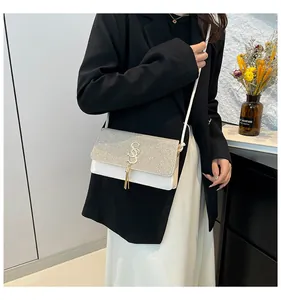 Détail d'un sac à bandoulière en cuir blanc avec rabat pailleté et pompon en métal doré