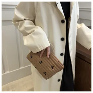 Detailaufnahme einer braun gesteppten Kosmetiktasche mit Schleifenstickerei am Model