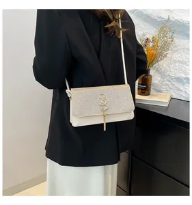 Détail du sac à bandoulière crème avec rabat pailleté et breloque à pompon doré