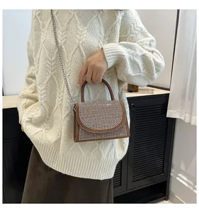Brown handbag with sparkling crystal flap and metal chain shown on beige sweater
