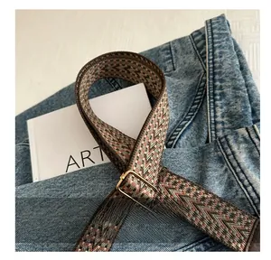 Macro detail of geometric woven strap with gold adjustable buckle on blue denim