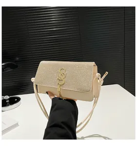 Détail du sac à bandoulière beige à strass avec logo SS doré et pompons métalliques