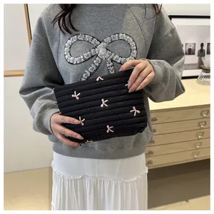 Detail der gesteppten schwarzen Kosmetiktasche mit rosa Bogen-Stickerei am Modell