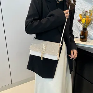 Sac bandoulière blanc à paillettes argentées et gland doré porté par un mannequin