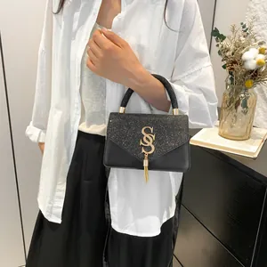 Sac à main chic en cuir noir avec rabat pailleté et ornement à pompon doré en S