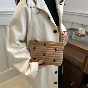 Braune gesteppte Kosmetiktasche mit Blumenstickerei, von einem Model in Trenchcoat gehalten