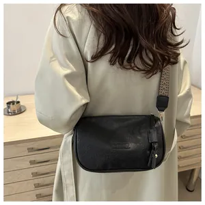 Detail of black pillow crossbody bag with FASHION embossing and wide geometric strap