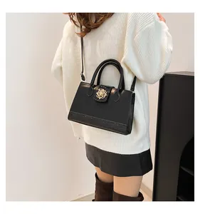Detail of black crossbody bag with faux crocodile texture and golden floral clasp