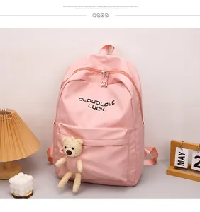 Détail d'un sac à dos rose en nylon avec lettrage noir et un charmant petit ours en peluche