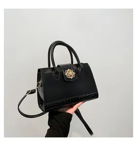 Detail of black faux leather handbag with crocodile pattern and golden flower buckle