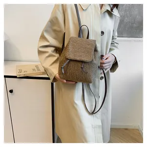 Brown fuzzy miniature backpack shown on beige coat, featuring drawstring and leather straps