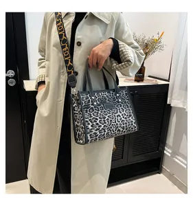 Detalle de bolso tote de leopardo con asas de cuero y correa ancha estampada