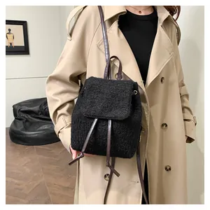 Detail of black fleece backpack with brown leather drawstrings worn on khaki trench coat