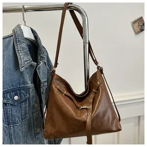 Detail view of coffee brown retro tote bag with golden buckles and denim jacket backdrop