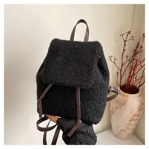 Detail of plush black mini backpack with brown leather straps in a cozy home setting