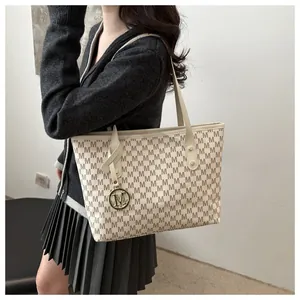 Detailed view of cream tote bag with brown monogram pattern and gold metal charm