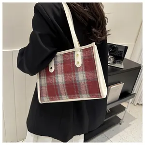 Detail view of red plaid tote bag with cream leather trim and slim shoulder straps