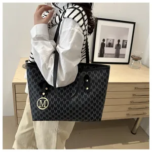 Detailed close-up of the black monogram tote bag with gold M-logo charm and dual straps